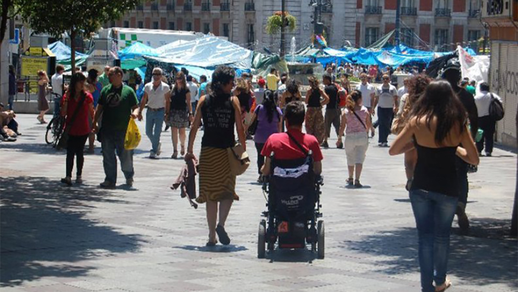 Hombre en silla de ruedas en medio de una calle concurrida